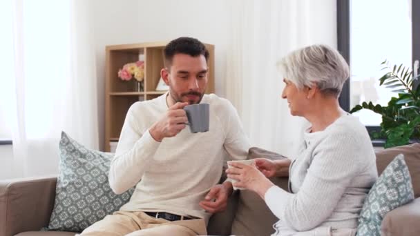 Hijo adulto y madre mayor beben café en casa — Vídeos de Stock