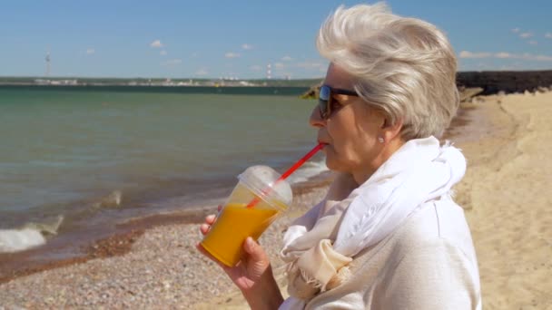 Senior woman drinking shake on summer beach — Stock Video