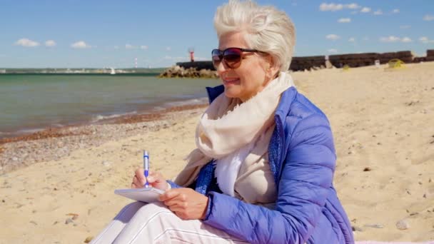 Senior woman writing to notebook on summer beach — Stock Video