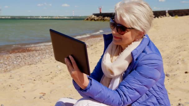 Senior vrouw met Tablet computer op het strand — Stockvideo