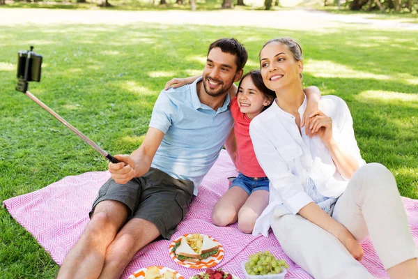 Familia haciendo picnic y tomando selfie en el parque —  Fotos de Stock