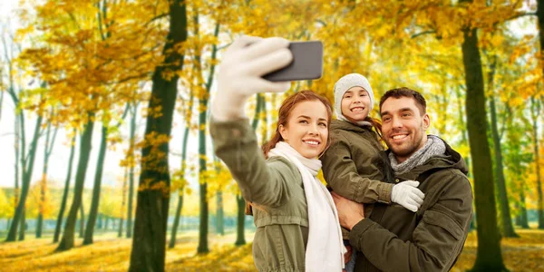 Семья делает селфи на смартфоне в осеннем парке — стоковое фото