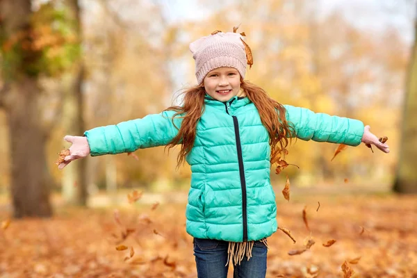 Счастливая девочка, играющая с листьями в осеннем парке — стоковое фото