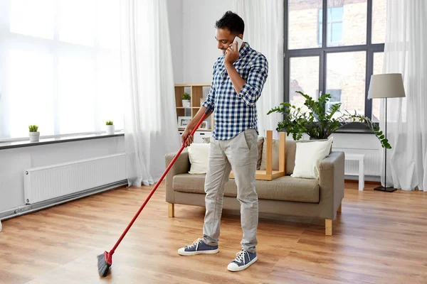 man with broom cleaning and calling on smartphone