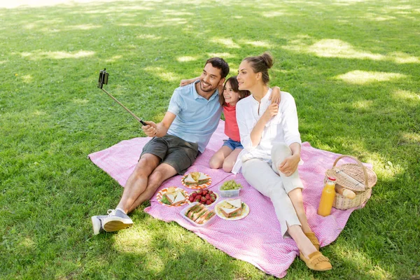 Familia haciendo picnic y tomando selfie en el parque —  Fotos de Stock