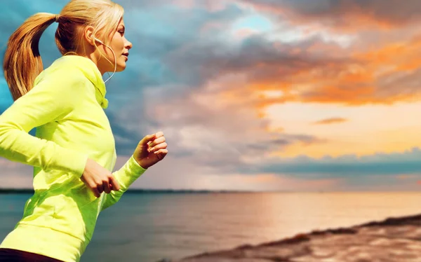 Mujer con auriculares corriendo sobre el atardecer del mar — Foto de Stock