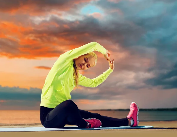 Kvinna stretching på träningsmatta vid havet — Stockfoto