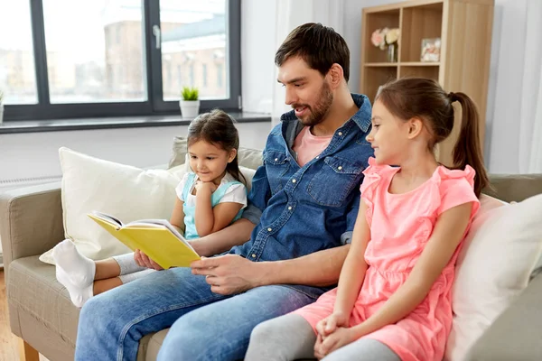 Glücklicher Vater mit Töchtern, die zu Hause Buch lesen — Stockfoto