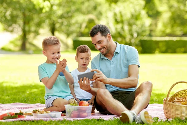 Família com smartphone fazendo piquenique no parque — Fotografia de Stock