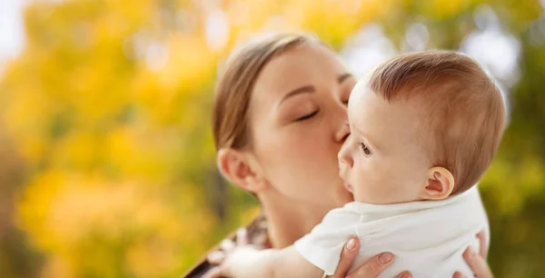 Gelukkig jonge moeder zoenen kleine baby in de herfst — Stockfoto