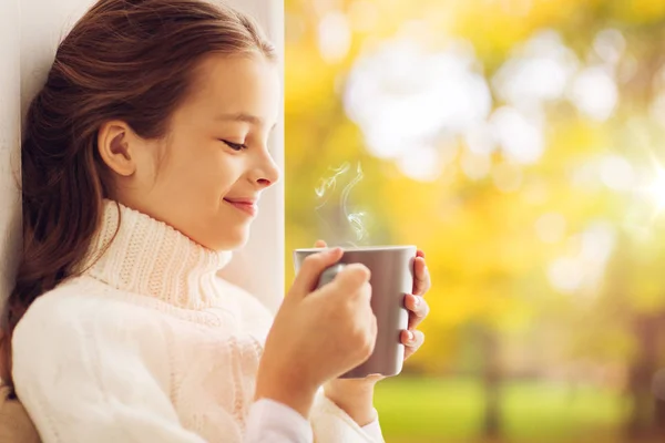 Девушка с кружкой чая сидя у окна дома осенью — стоковое фото