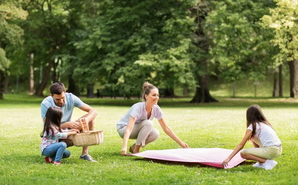 Семья кладет одеяло для пикника в летнем парке — стоковое фото
