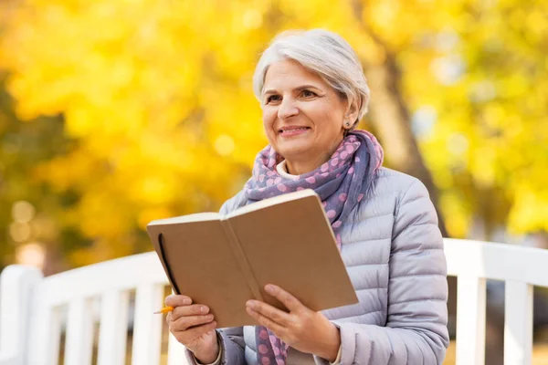Wanita senior yang bahagia membaca buku harian di taman musim gugur — Stok Foto
