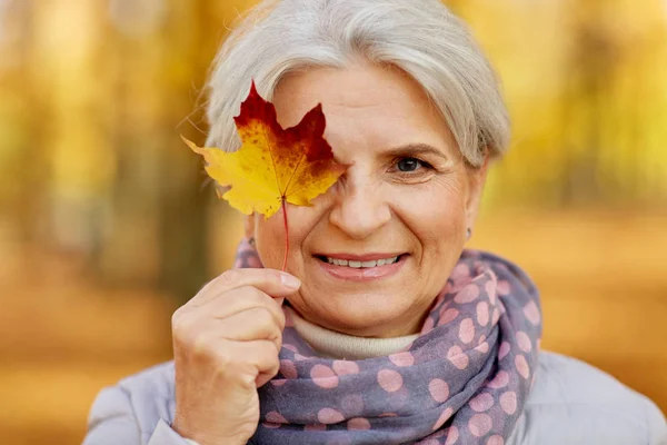 Ευτυχισμένη ανώτερη γυναίκα με το φύλλο σφενδάμου στο φθινόπωρο πάρκο — Φωτογραφία Αρχείου