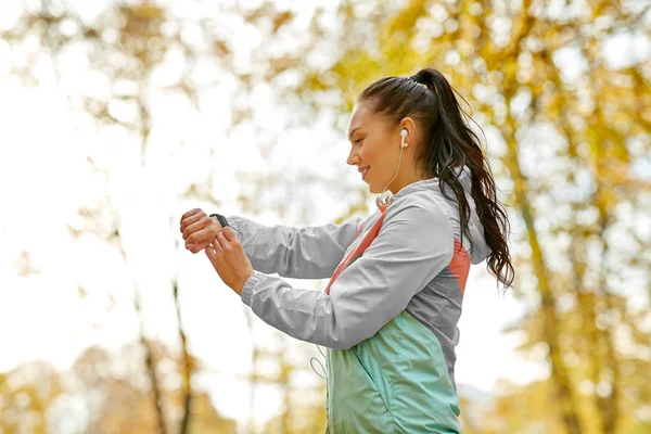 Frau schaut sich Fitness-Tracker im Herbstpark an — Stockfoto