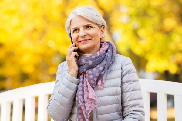 Пожилая женщина звонит на смартфон в осеннем парке — стоковое фото