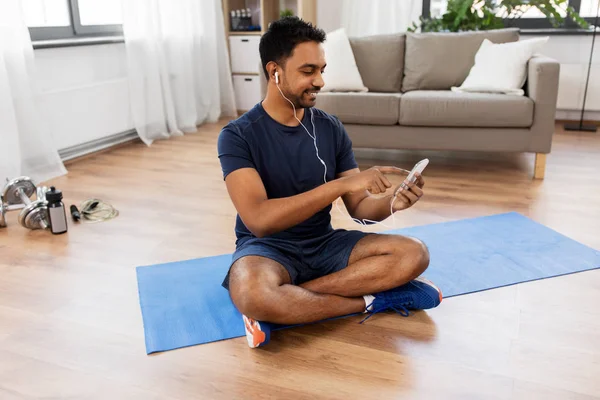 Hombre indio con teléfono inteligente en alfombra de ejercicio en casa —  Fotos de Stock