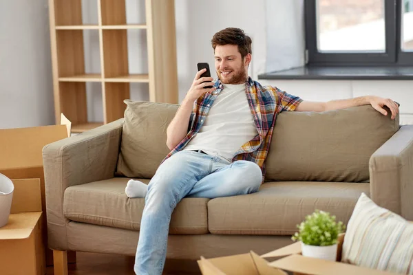 Homme avec smartphone et boîtes sur canapé à la nouvelle maison — Photo