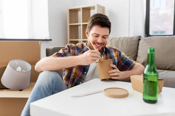 Glimlachende man eet afhaaleten in nieuw huis — Stockfoto