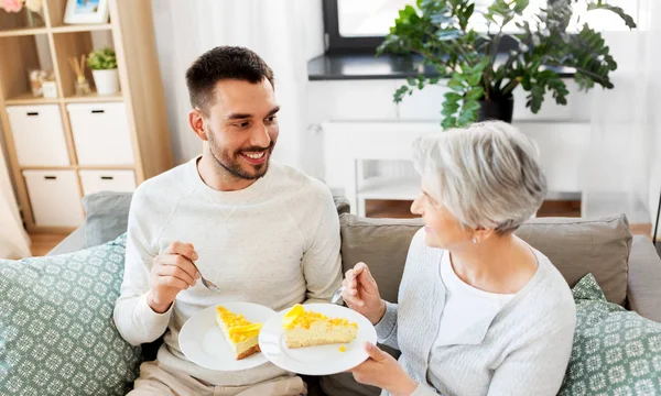 Senior mother and adult son eating cake at home — Stock Photo, Image