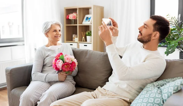 Yetişkin bir çocuk, yaşlı bir annenin fotoğrafını çekiyor. — Stok fotoğraf