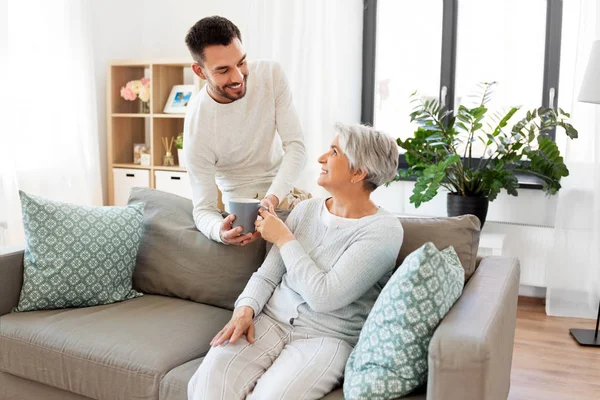 Volwassen zoon brengt koffie naar senior moeder thuis — Stockfoto