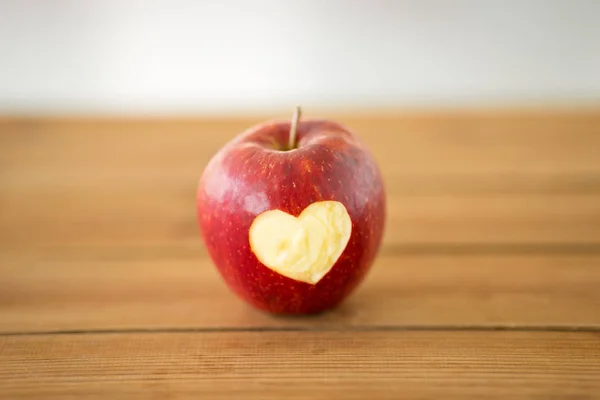 Roter Apfel mit geschnitzter Herzform auf Holztisch — Stockfoto