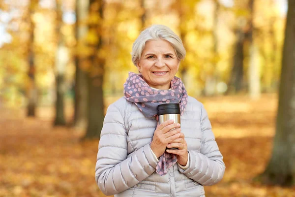Пожилая женщина с горячим напитком в тумблере в осеннем парке — стоковое фото
