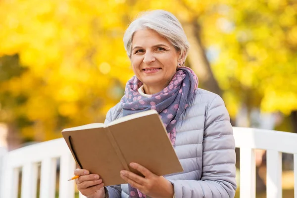 Happy senior woman reading diary at autumn park — Stock Photo, Image