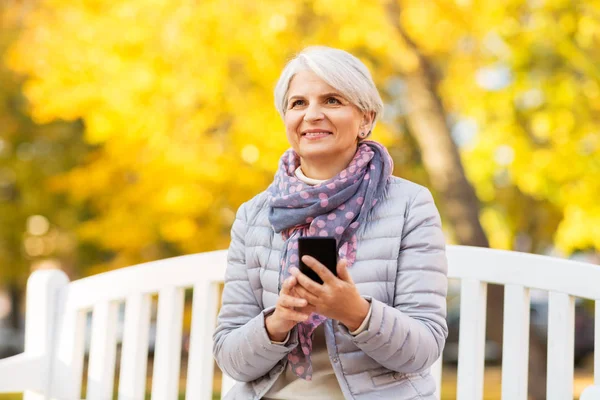 Boldog idős nő okostelefonnal őszi park — Stock Fotó