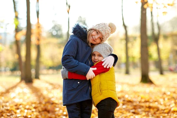Happy children hugging at autumn park — Stock Photo, Image