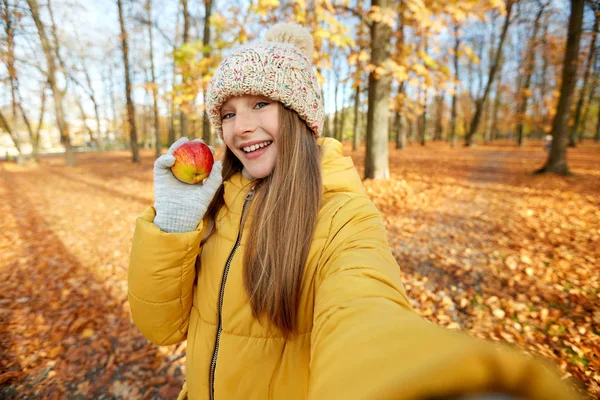 Menina feliz com maçã tomando selfie no parque de outono — Fotografia de Stock