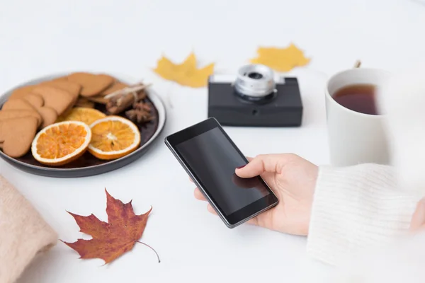 Mão com smartphone, chá e folhas de outono — Fotografia de Stock