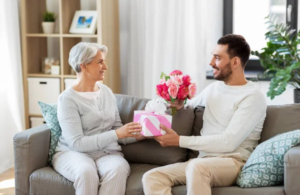 Hijo dando regalo y flores a la madre mayor — Foto de Stock