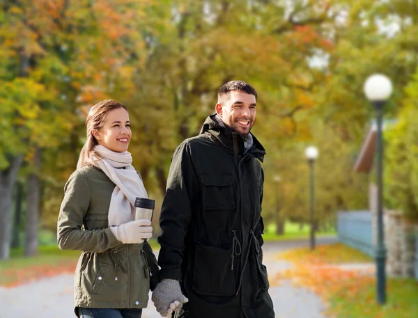 Couple with tumbler walking along autumn park — Stock Photo, Image