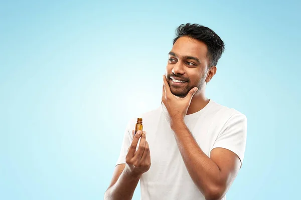 Smiling indian man applying grooming oil to beard — Stock Photo, Image