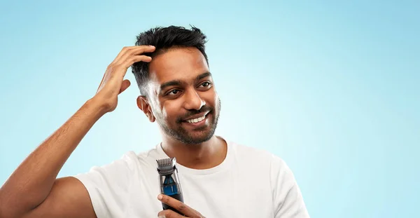 Улыбающийся индийский мужчина с триммером, трогающий свои волосы — стоковое фото