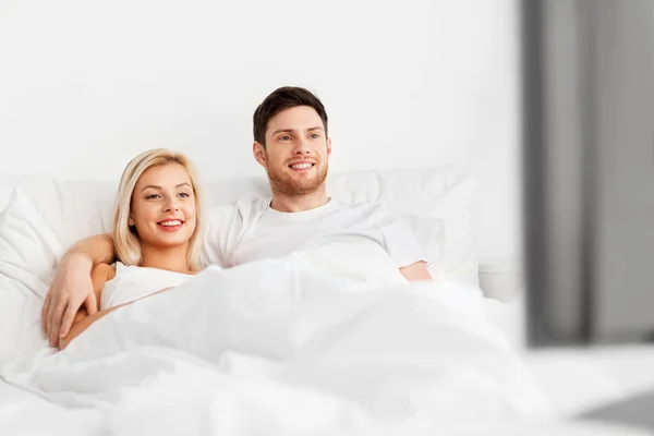 Happy couple lying in bed at home and watching tv — Stock Photo, Image