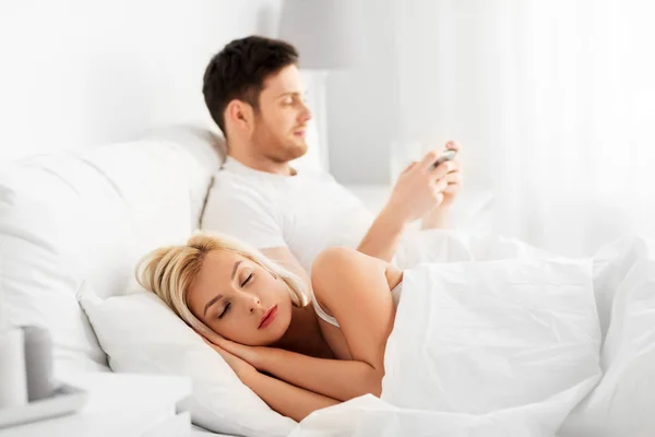 Hombre usando el teléfono inteligente mientras la mujer está durmiendo — Foto de Stock