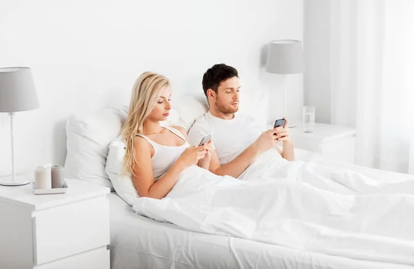 Pareja con smartphones en la cama — Foto de Stock