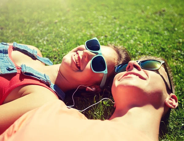 Feliz pareja adolescente con auriculares tumbados en la hierba —  Fotos de Stock