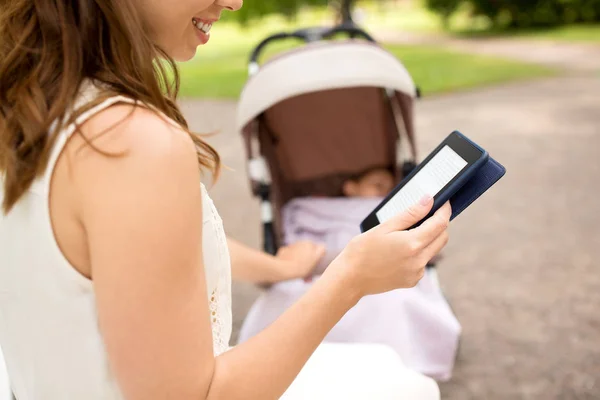 Mamma med barnvagn läser internet bok i parken — Stockfoto