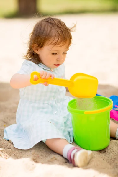 Pequena menina brinca com brinquedos em sandbox — Fotografia de Stock