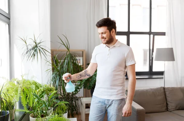 Homem pulverizando plantas de sala com água em casa — Fotografia de Stock