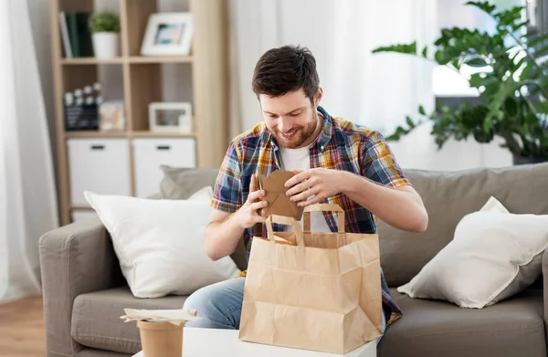 Hombre sonriente desempacando comida para llevar en casa — Foto de Stock