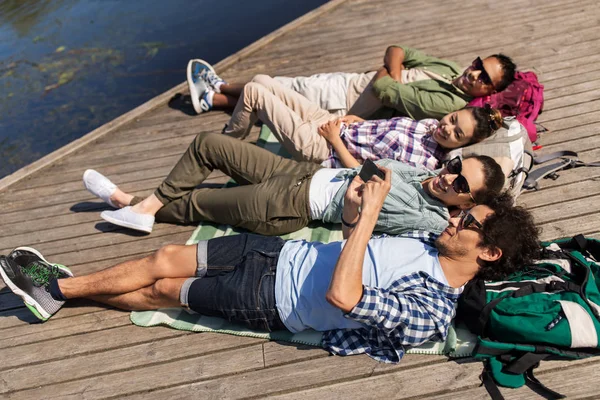 Vrienden met smartphone liggend op de pier van het meer — Stockfoto