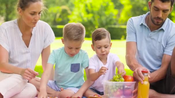 Счастливая семья ест фрукты на пикнике в парке — стоковое видео