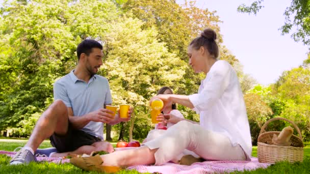 Счастливая семья пьет сок на пикнике в парке — стоковое видео