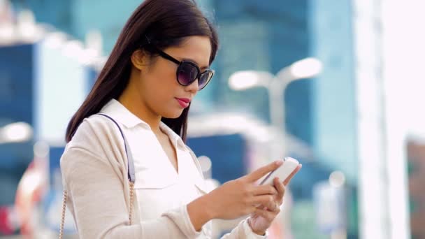 亚洲妇女在太阳镜使用智能手机在城市 — 图库视频影像