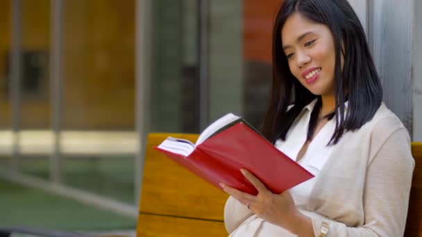 Sorridente asiatico donna lettura libro seduta su panchina — Video Stock